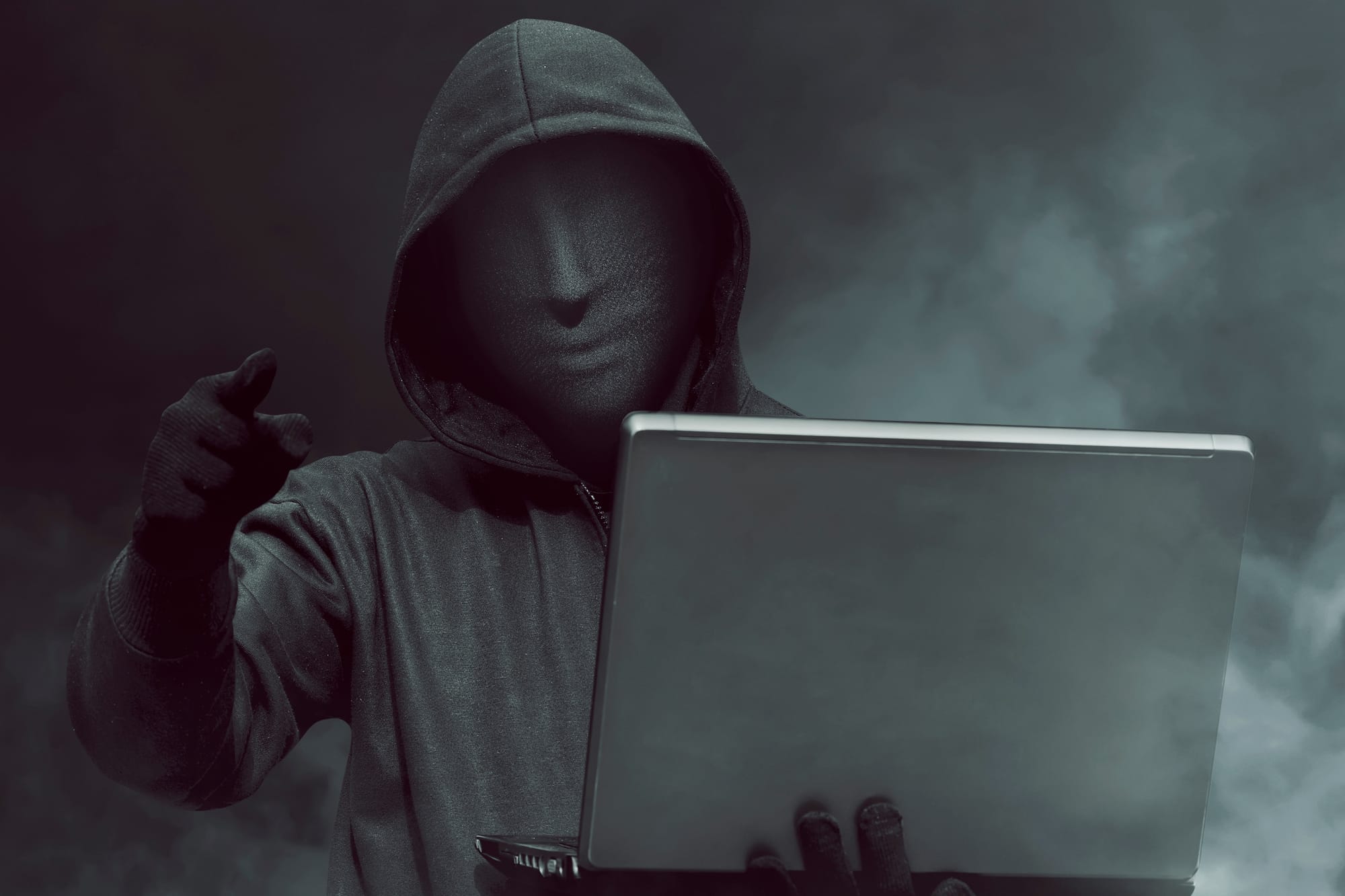 portrait-hooded-hacker-with-mask-holding-laptop-while-standing.jpg